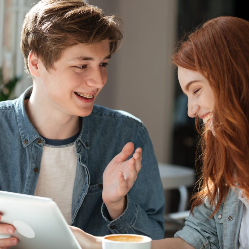Young smiling couple talking while using tablet in cafe